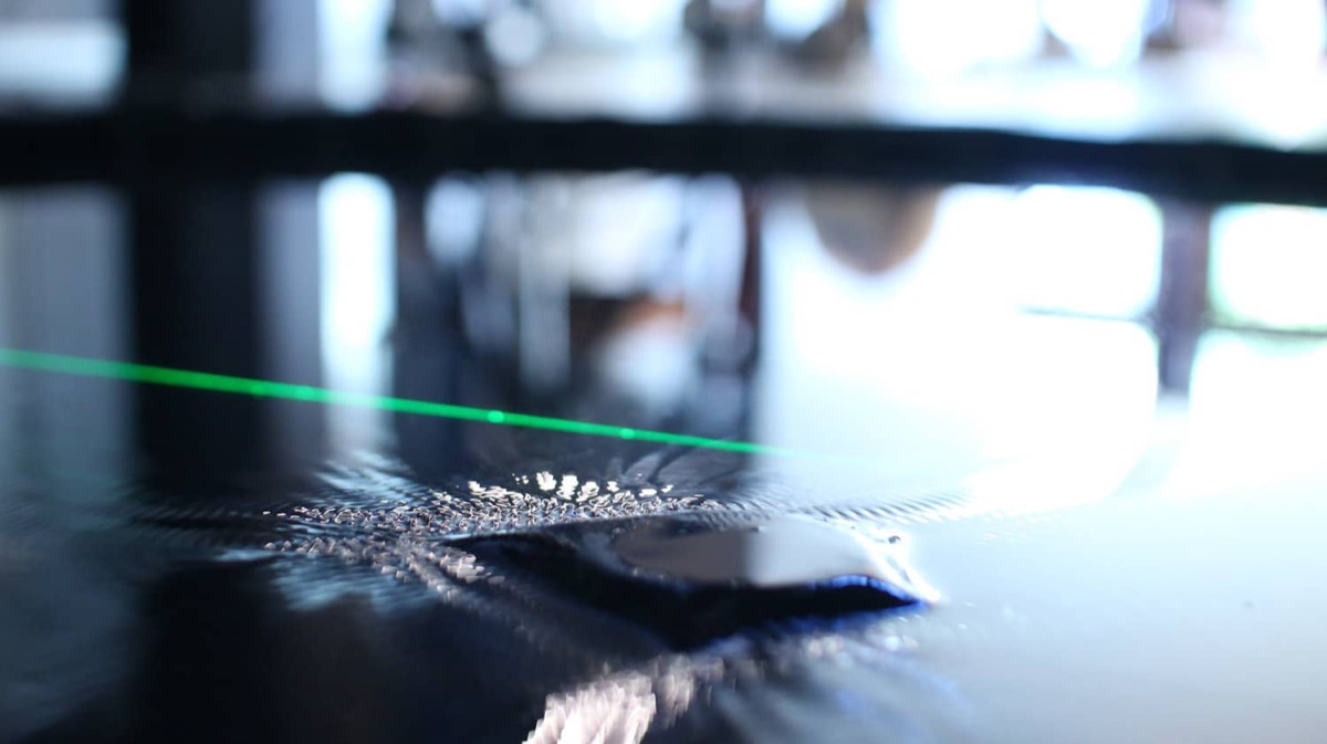 A close-up of the water surface with the green laser line skimming across it, ripples textured by the transducer below.