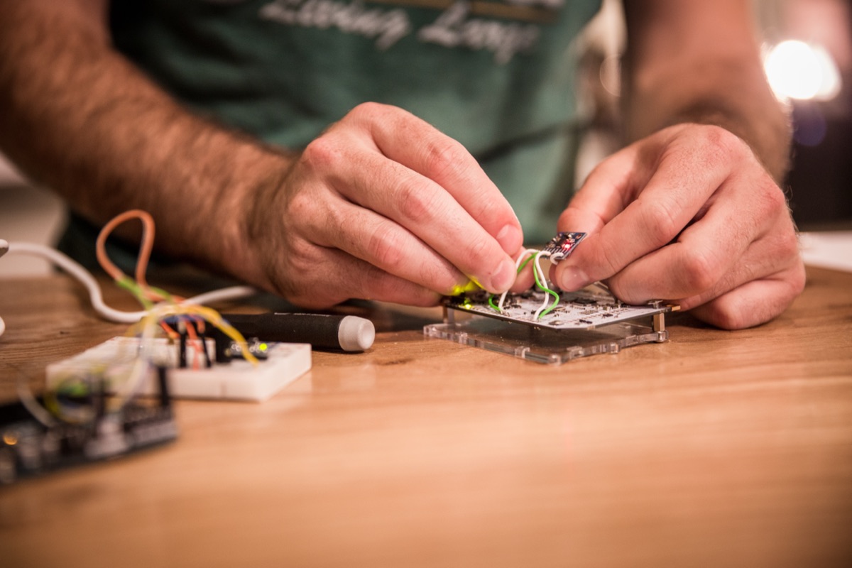 Hands wiring a small accelerometer breakout board on the workbench — the sensor for the curved-steel piece.