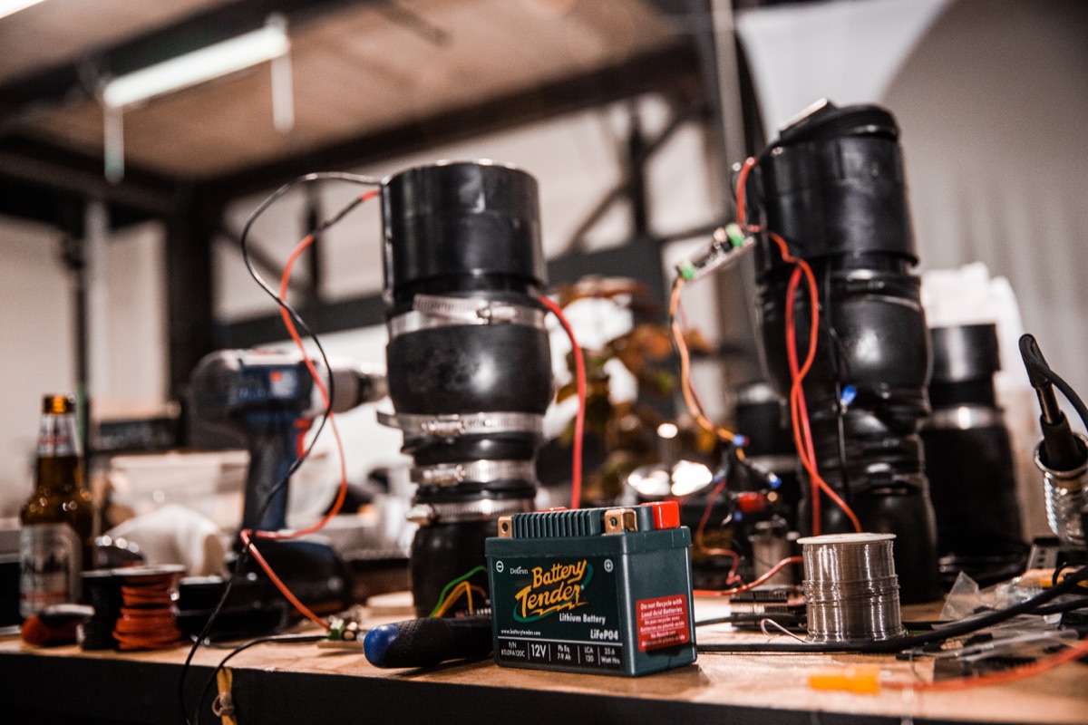 A row of finished actuator assemblies on the bench with a 12V battery and red power leads — the drivers that made the innertube sculpture move when the bus arrived.