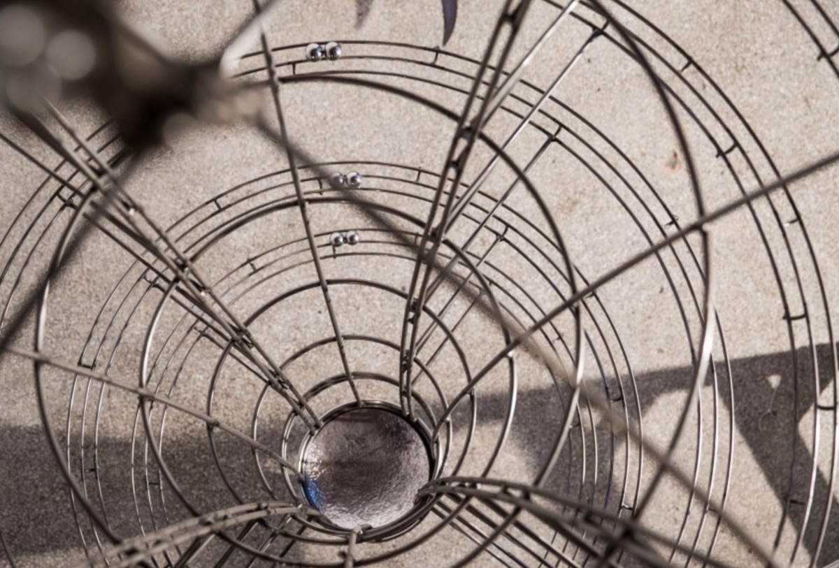 Looking down through the concentric wire bands of a spinning top, with steel ball bearings traveling its tracks.