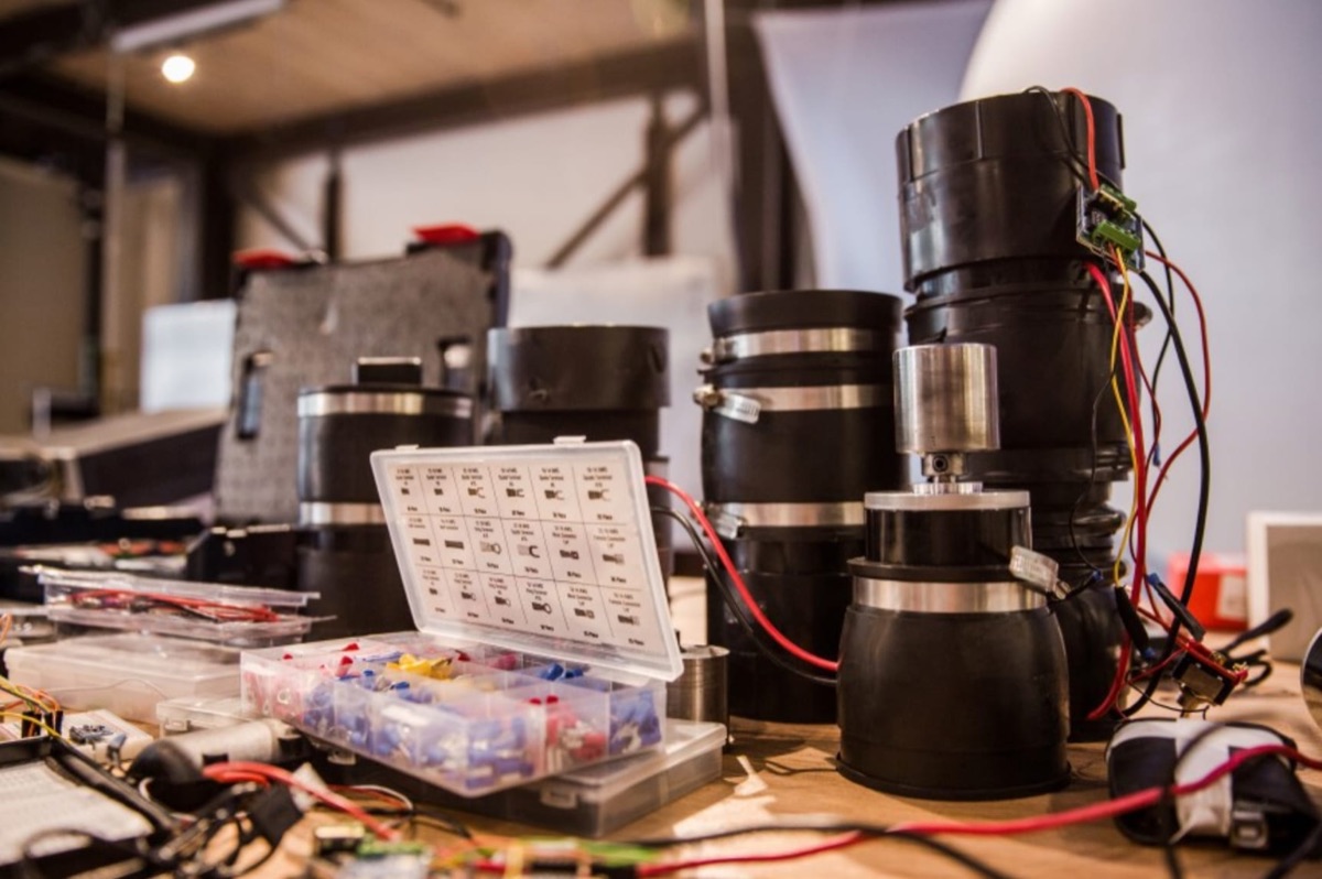 Workbench detail: black actuator housings, sorted electrical connectors, and wire harnesses being assembled for the innertube sculpture's bus-response drive.